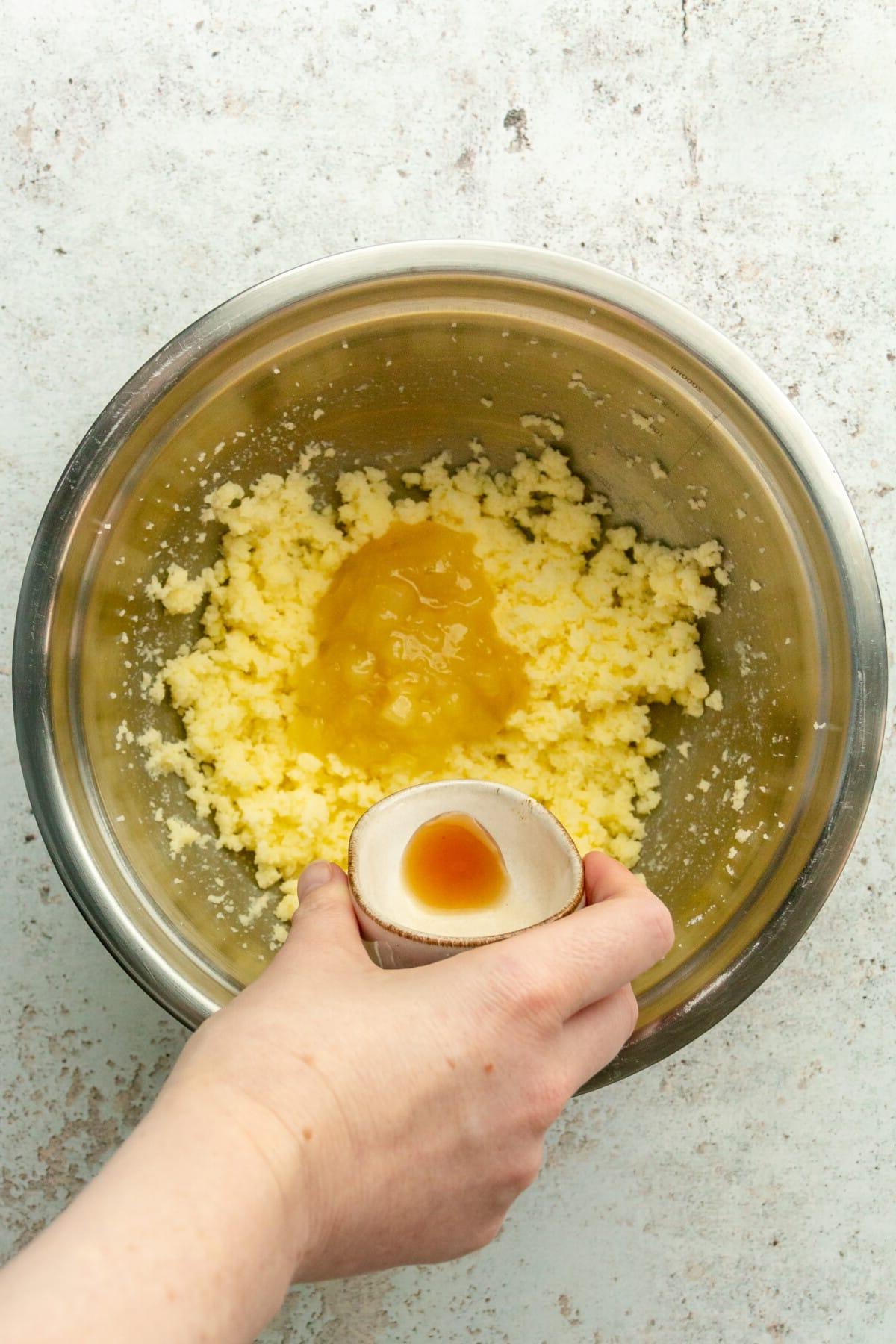 **Weiße Schokoladen-Pfefferminz-Kühlschrankkekse** 6 Vanilleextrakt wird über geschlagene Butter und Apfelmus in einer Edelstahlschüssel auf hellem grauem Untergrund gegeben.