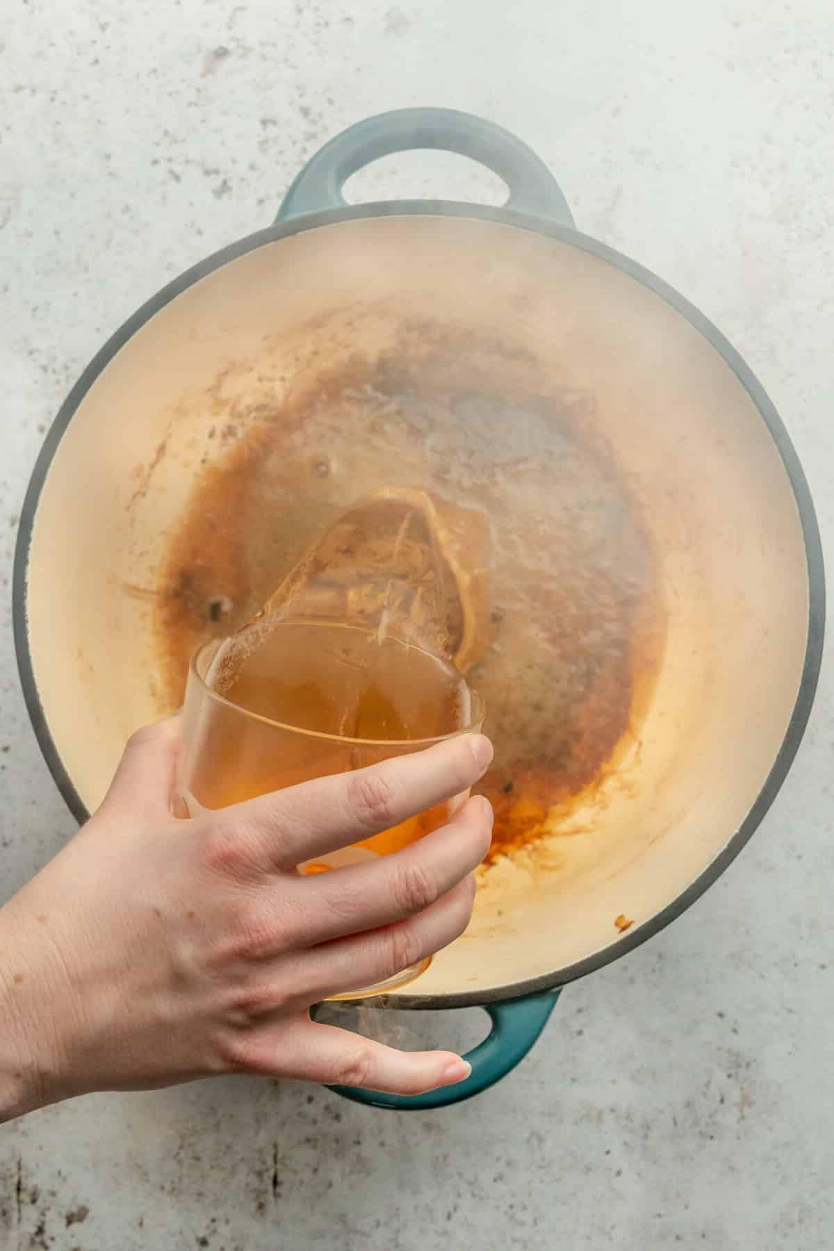 Apfelwein-Schweinebraten 6 Apfelwein wird in einen heißen Bräter auf einer hellgrauen Oberfläche gegossen.