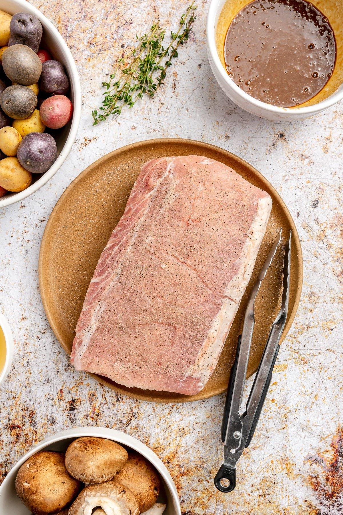 **Balsamico-Schweinelendenrezept** 6 Die Gewürzmischung wurde auf die Oberfläche eines Schweinefilets gerieben, das auf einem braunen Teller liegt. Eine schwarze Zange liegt daneben.