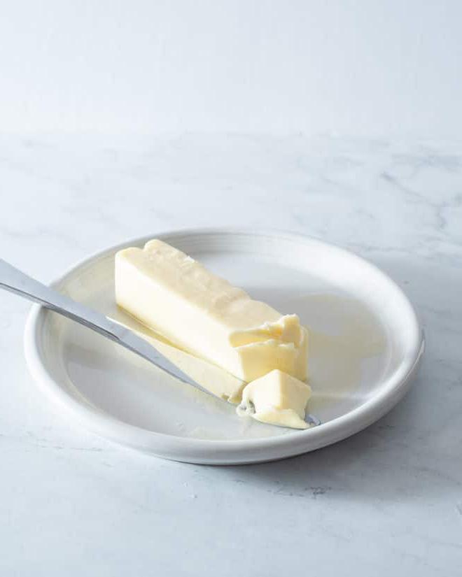 Butter schnell weich bekommen 3 Ein Stück weiche Butter auf einem kleinen weißen Teller mit einem Buttermesser daneben
