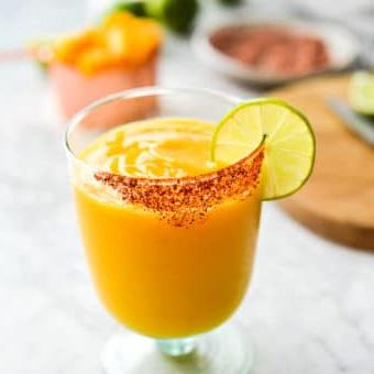 Einfaches Mango-Margarita-Rezept (Gefroren und auf Eis) 7 Ein Glas Frozen Mango Margarita mit Chilischnee-Rand, Zutaten für Mango Margaritas im Hintergrund