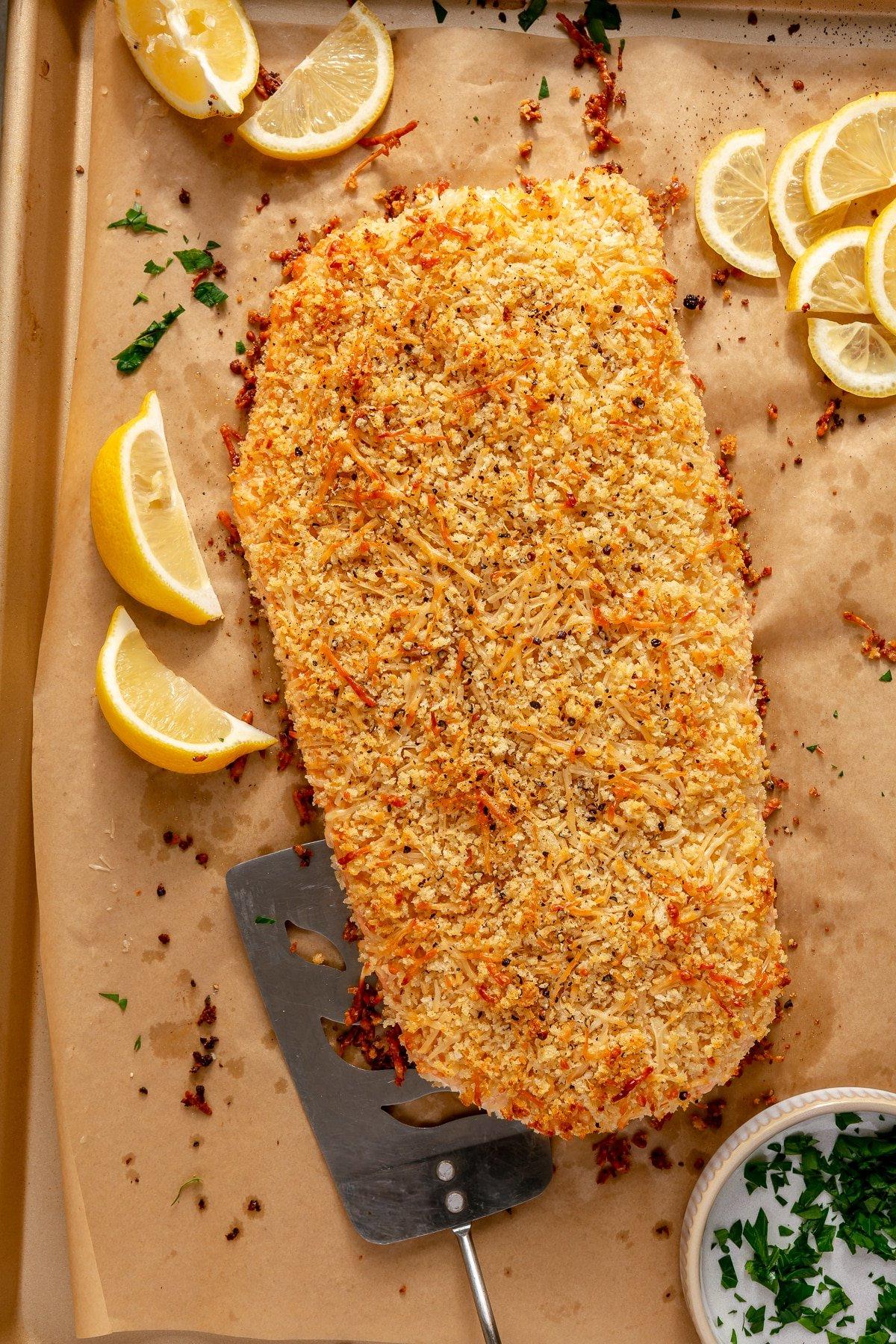 Lachs mit Parmesankruste 7 Ein Teller mit dem fertigen gebackenen Parmesan-Lachs, garniert mit Zitrone und Petersilie.
