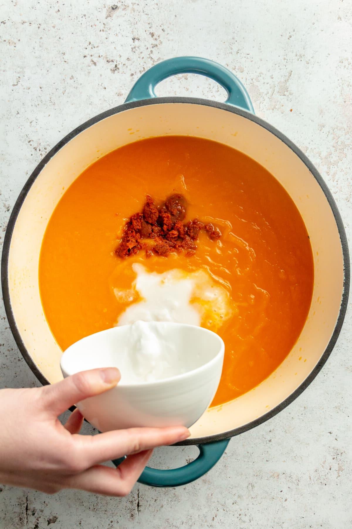 Thailändische Karotten-Ingwer-Suppe 7 Eine Person gibt Kokosmilch in einen Topf mit Karottensuppe.