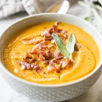 Graue Schüssel mit Instant Pot Kürbissuppe, belegt mit Speck und Salbei, auf einem Marmorbrett