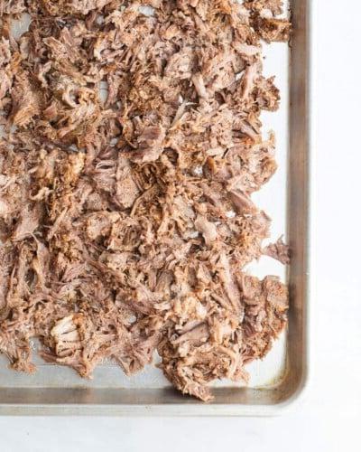 Ein Backblech mit gewürztem, zerkleinertem Schweinefleisch, bevor es in den Ofen kommt, um Carnitas zu machen