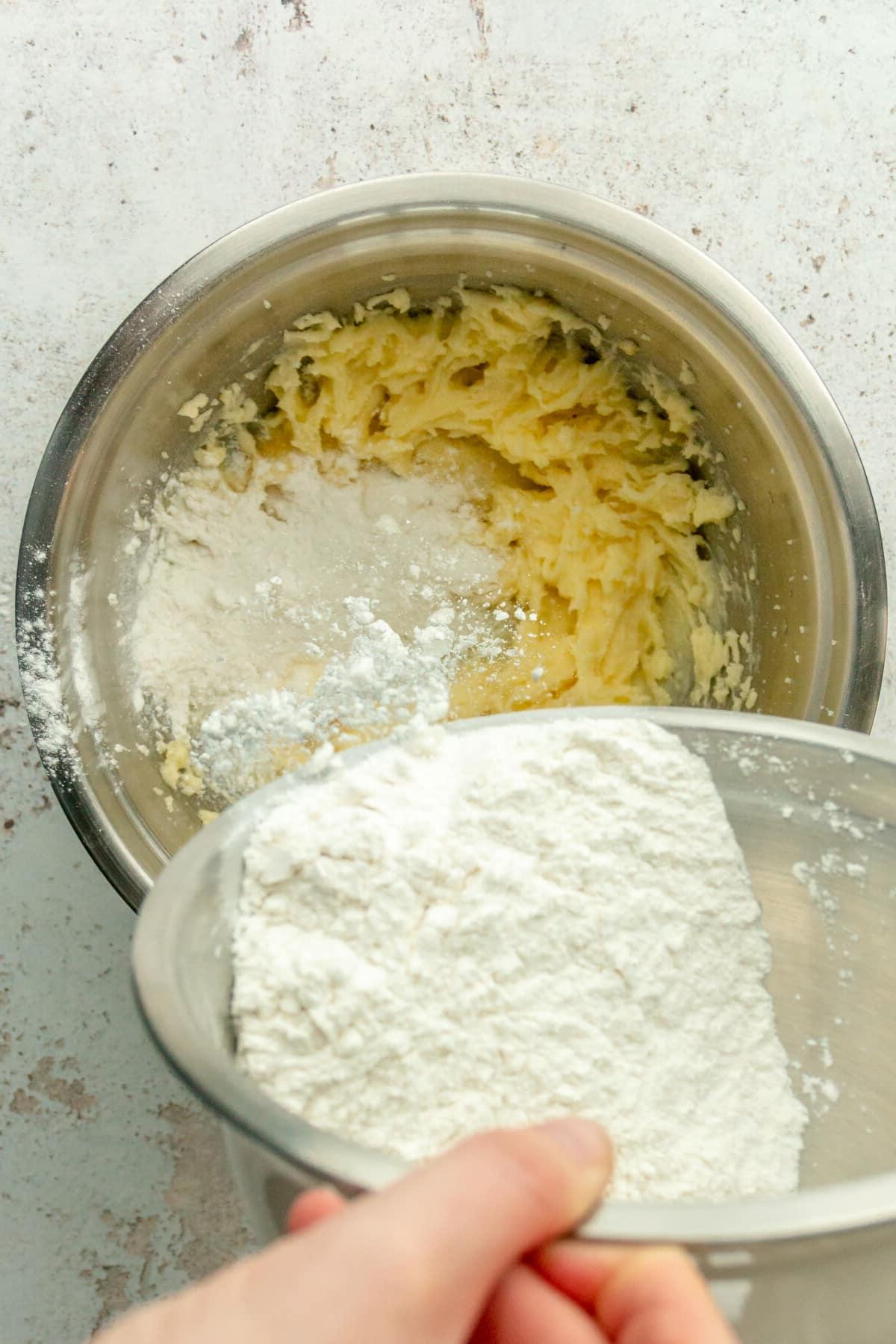 **Weiße Schokoladen-Pfefferminz-Kühlschrankkekse** 7 Eine Mischung aus Mehl und Triebmitteln wird in eine geschlagene Butter-Zucker-Mischung in einer Edelstahlschüssel auf hellem grauem Untergrund gegeben.