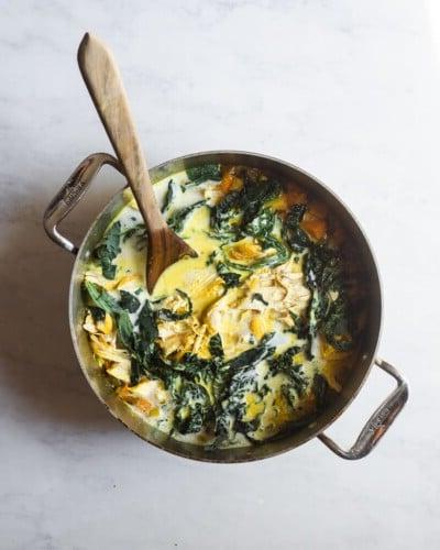 210423_Healing Tumeric Soup-27 Ein großer Topf mit heilender Kurkuma-Hühnersuppe und einem Holzlöffel darin