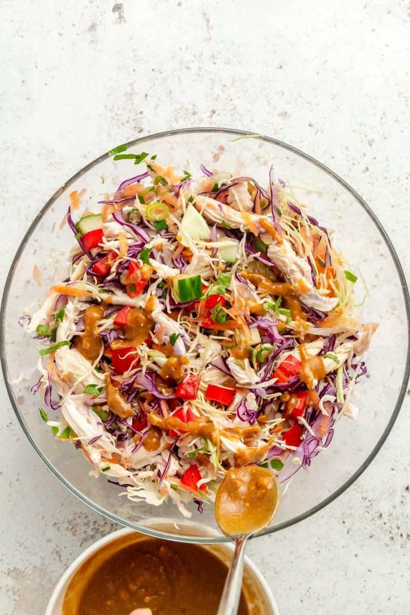 Thai-inspirierter Erdnuss-Hähnchensalat 7 Thai-inspirierter Hähnchensalat in einer großen Glasschüssel. Eine braune Sauce wird darüber geträufelt.