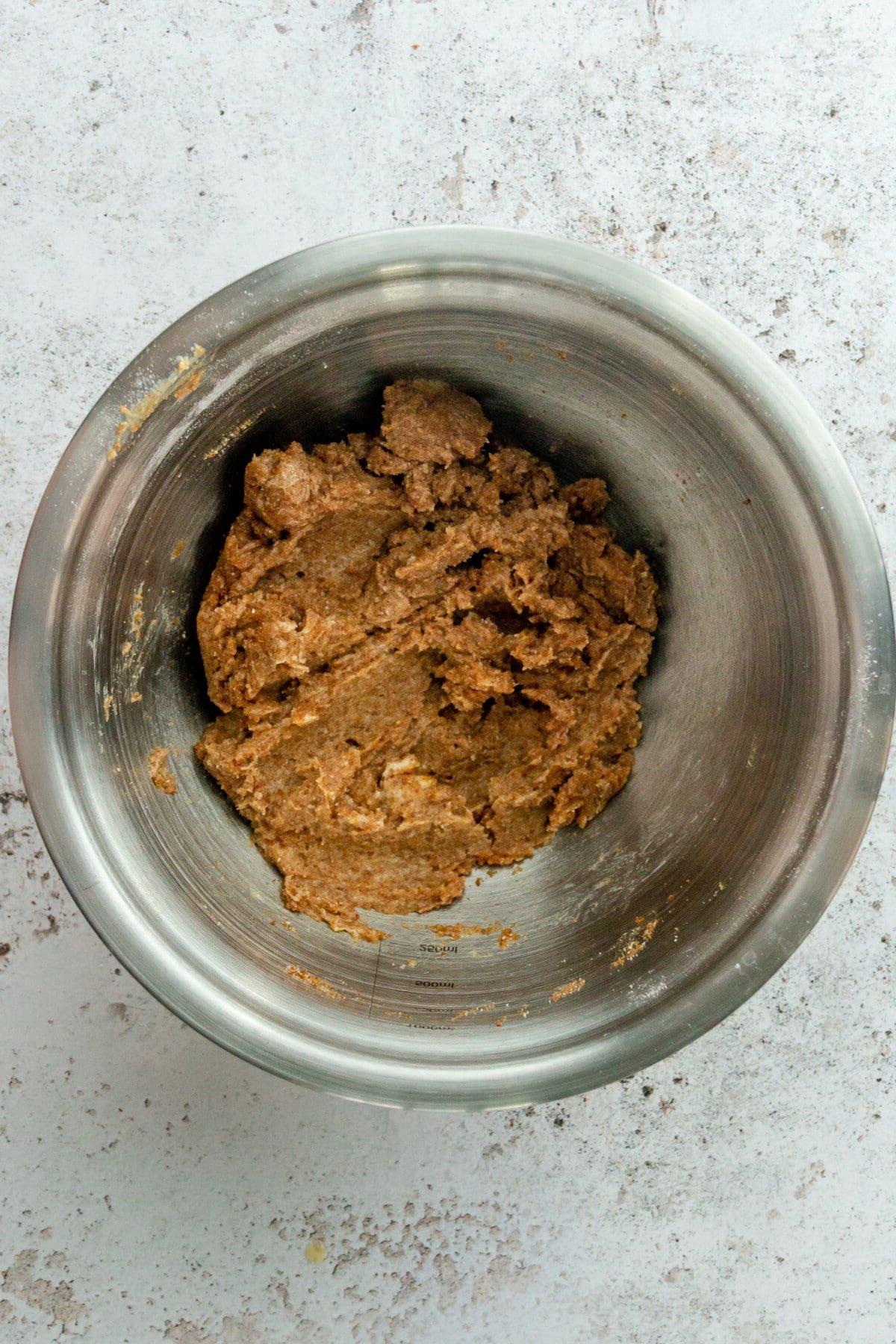 **Paläo Apfel-Zimt-Muffins** 7 A crumble mixture sits in a stainless steel bowl on a light gray surface.