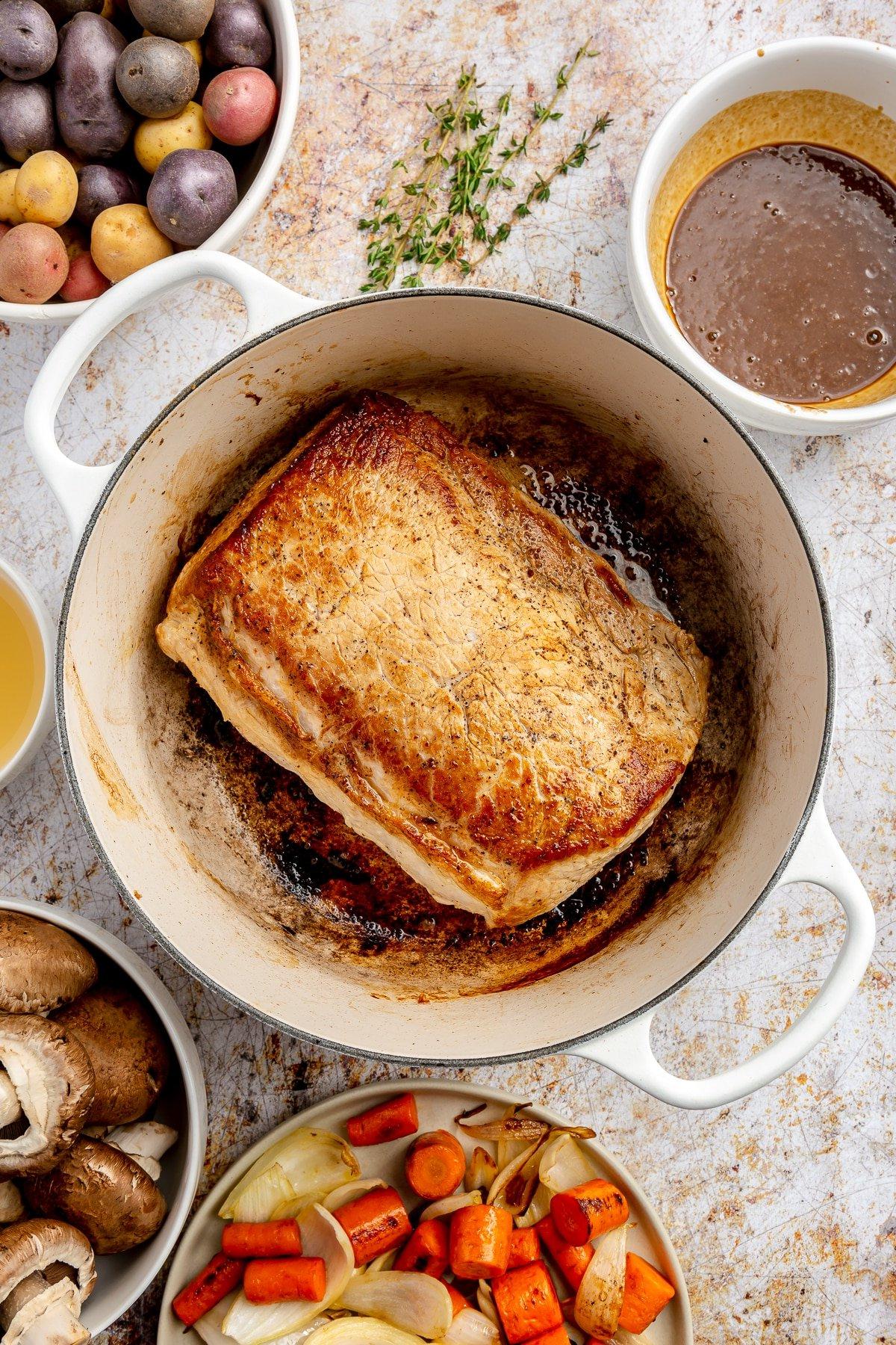 **Balsamico-Schweinelendenrezept** 7 Das halb gegarte Schweinefilet, jetzt goldbraun, liegt in einem weißen, emaillierten Topf.
