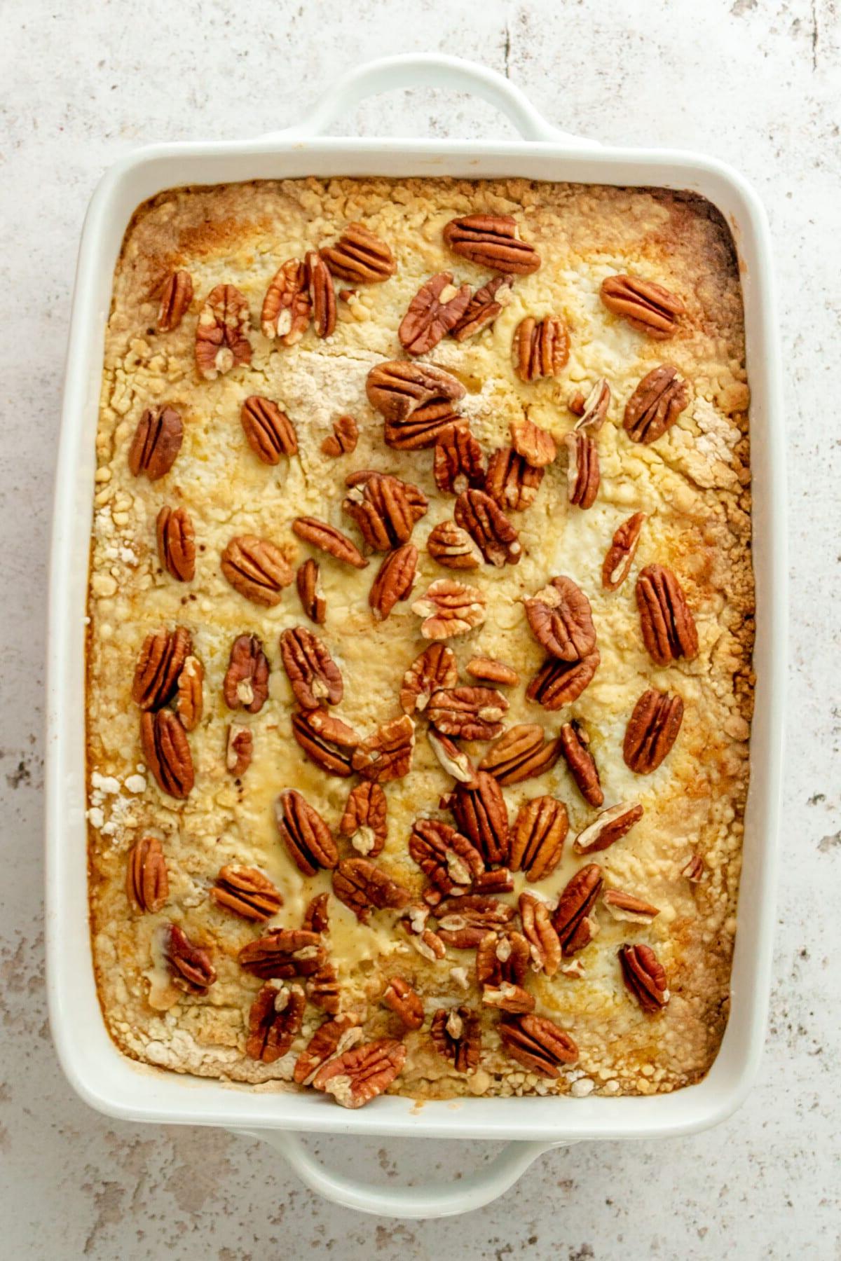 Kürbis-Dump-Kuchen 7 Pekannüsse liegen auf einem Kürbis-Dump-Cake in einer weißen, rechteckigen Auflaufform auf hellgrauem Untergrund.