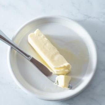 Butter schnell weich bekommen 4 Ein Stück weiche Butter auf einem kleinen weißen Teller mit einem Buttermesser daneben