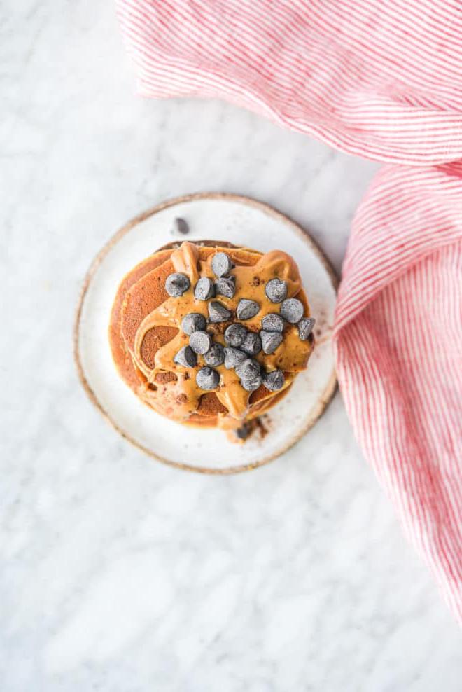 Wie man Protein-Pfannkuchen zubereitet 4 Eine Draufsicht auf einen Stapel Protein-Pancakes, garniert mit Erdnussbutter und Schokoladenstückchen.