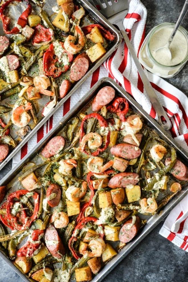 Cajun Garnelen vom Backblech 8 Draufsicht eines Ofenblechs beladen mit Wurst, Garnelen, Kartoffeln, Spargel und roten Paprika, übergossen mit einer cremigen Soße, auf einem dunkelgrauen Tisch mit rot gestreifter Serviette