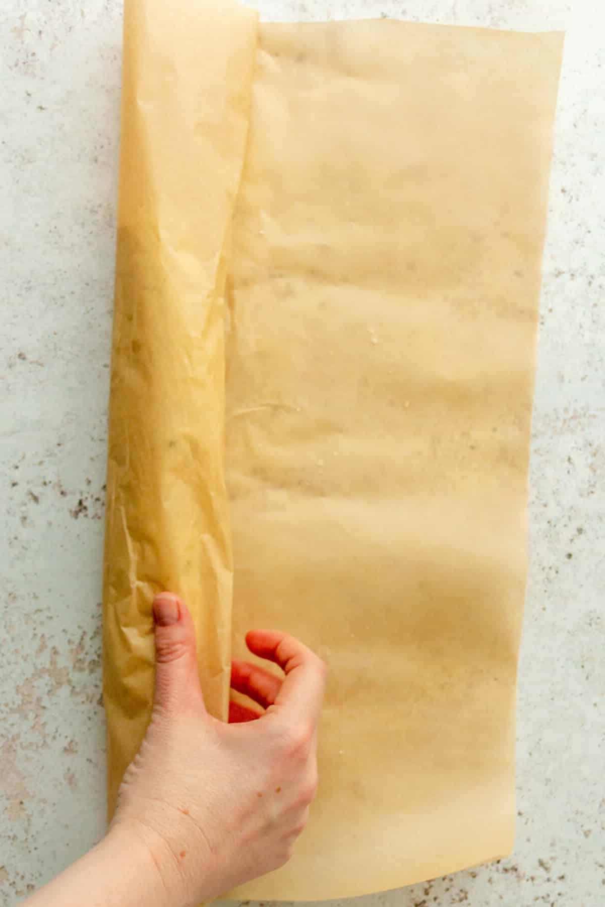**Weiße Schokoladen-Pfefferminz-Kühlschrankkekse** 8 Keksteig wird in Backpapier zu einer Rolle geformt auf hellem grauem Untergrund.