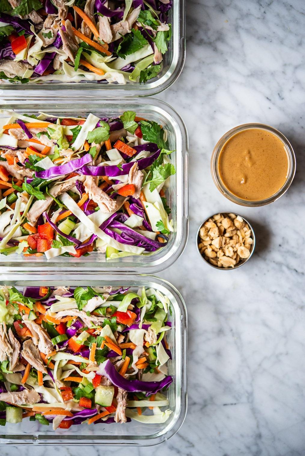 Thai-inspirierter Erdnuss-Hähnchensalat 8 Ein farbenfroher Thai-Hähnchensalat in 3 einzelnen Glas-Meal-Prep-Behältern neben Erdnussdressing und zerstoßenen Erdnüssen
