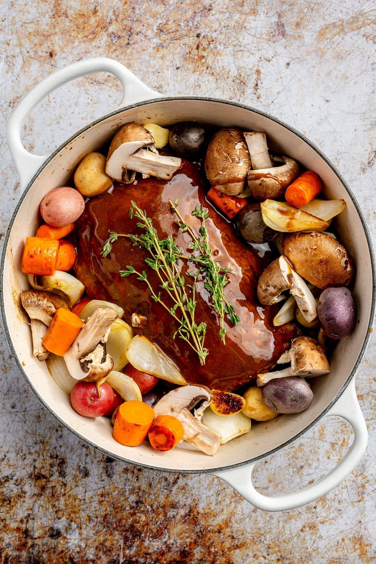 **Balsamico-Schweinelendenrezept** 8 Alle Zutaten liegen in einem großen, weißen, emaillierten Topf. Frische Thymianzweige ruhen obenauf.