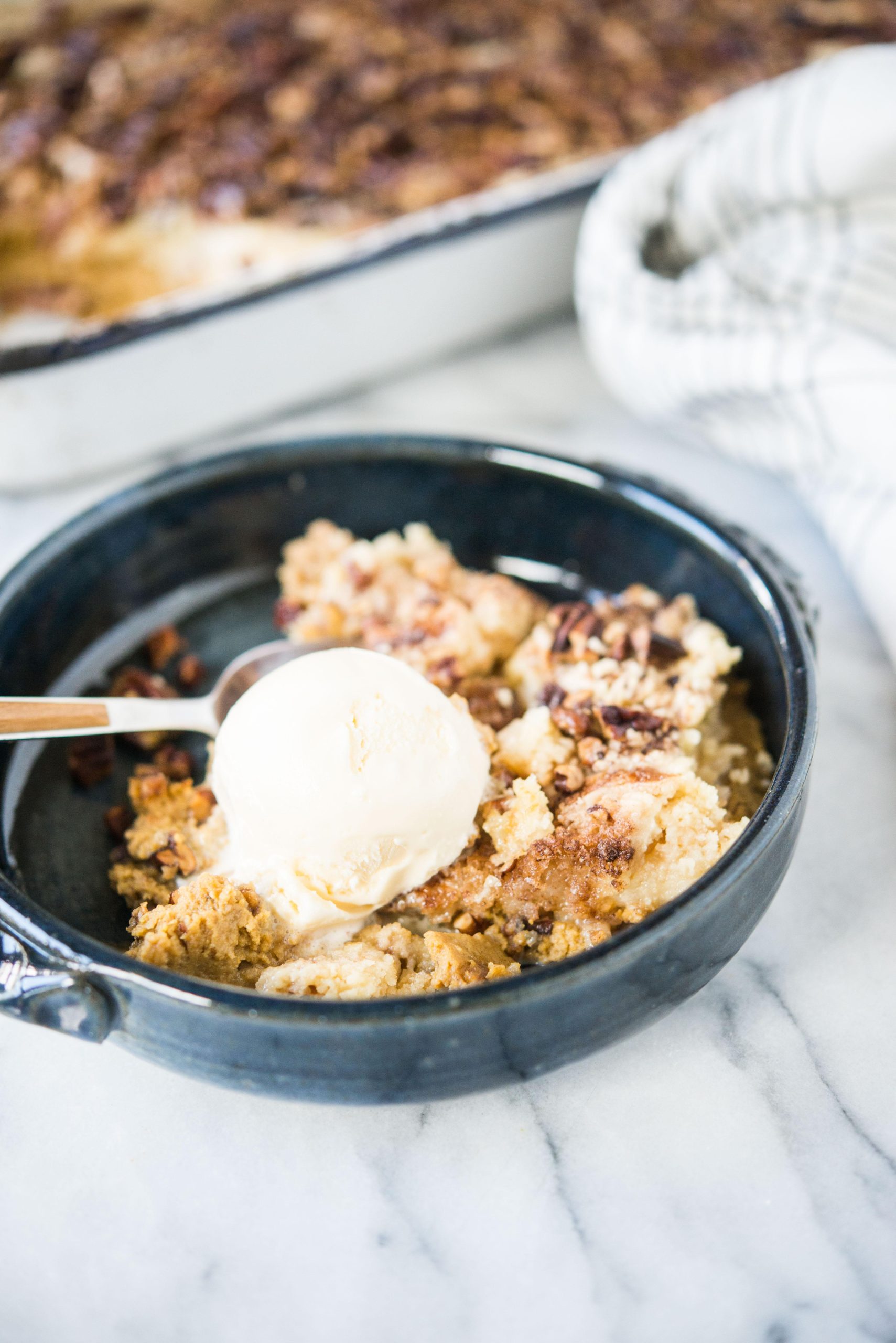 Kürbis-Dump-Kuchen 8 Dunkelblaue Schüssel mit Kürbis-Dump-Cake und einer Kugel Eiscreme darauf.