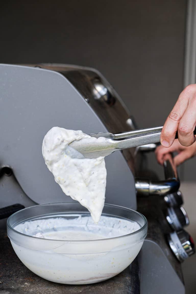 200724_SF Lemon Yogurt Chicken-05 In Zitronen-Joghurt marinierte Hähnchenbrust wird mit einer Zange gehalten und ist bereit für den Grill