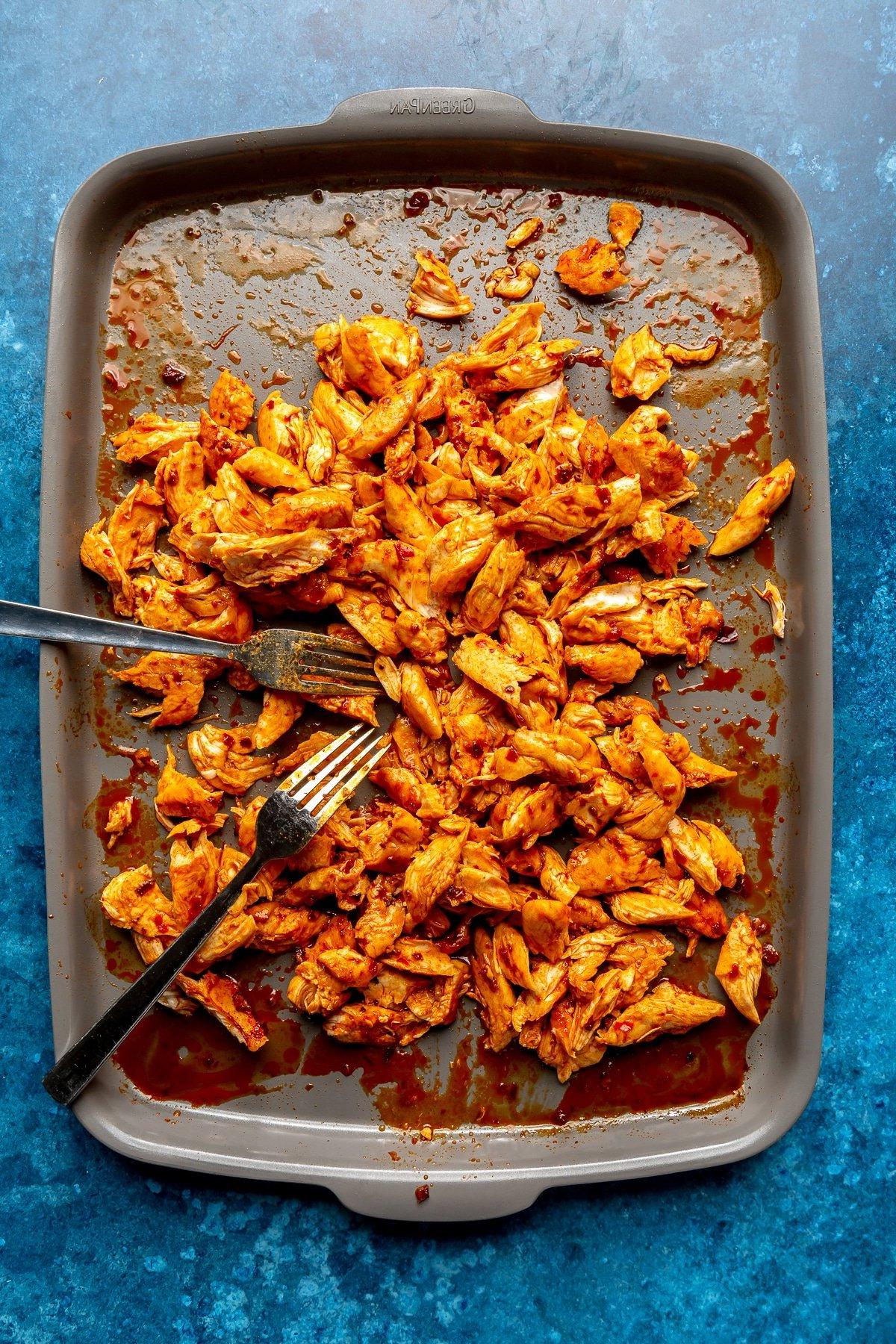 Harissa-Honig-Hähnchen-Bowls 8 Die gebackenen Hähnchenstücke werden mit zwei Metallgabeln zerkleinert.