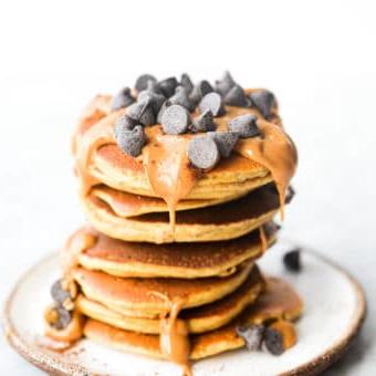 Wie man Protein-Pfannkuchen zubereitet 5 Ein Stapel Protein-Pancakes, garniert mit Erdnussbutter und Schokoladenstückchen.