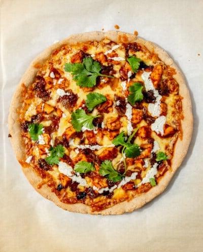 BBQ Hähnchen Pizza garniert mit Koriander und Ranch-Dressing vor dem Schneiden.