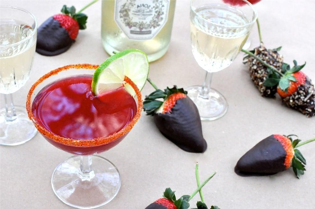 Zwei Granatapfel Martinis auf einem Holztisch, im Hintergrund unscharf die Umgebung.