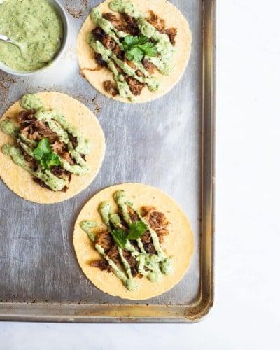 3 offene Carnitas Tacos, belegt mit cremiger Avocado-Verde-Sauce und Koriander, auf einem Backblech neben einer Schüssel cremiger Avocado-Verde-Sauce