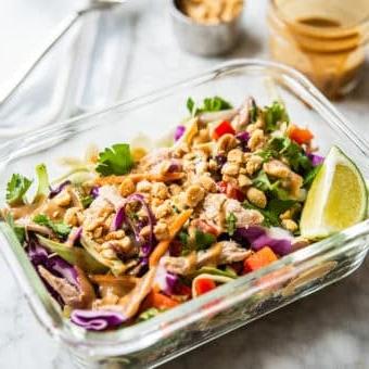 Thai-inspirierter Erdnuss-Hähnchensalat 9 Ein farbenfroher Thai-Hähnchensalat in einem einzelnen Glas-Meal-Prep-Behälter mit Erdnussdressing und zerstoßenen Erdnüssen im Hintergrund