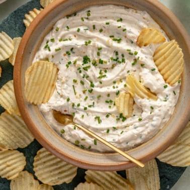 Eine große Schüssel Französischer Zwiebeldip, garniert mit frischem Schnittlauch und umgeben von Kartoffelchips.