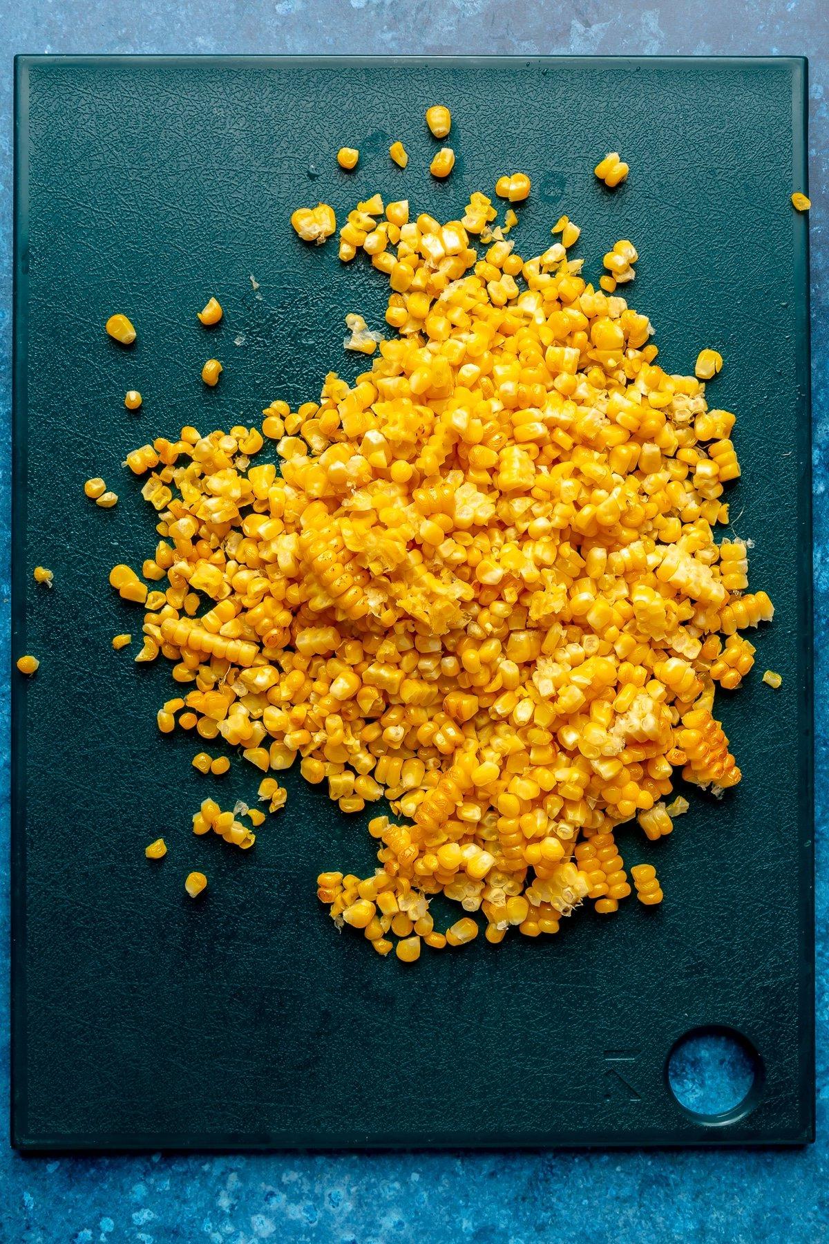 Harissa-Honig-Hähnchen-Bowls 9 Geröstete Maiskörner liegen auf einem dunkelblauen Schneidebrett.