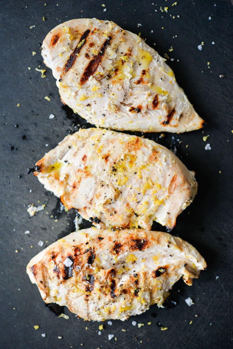 200724_SF Lemon Yogurt Chicken-13 Drei gegrillte Zitronen-Joghurt-Hähnchenbrüste ruhen auf einem schwarzen Schneidebrett