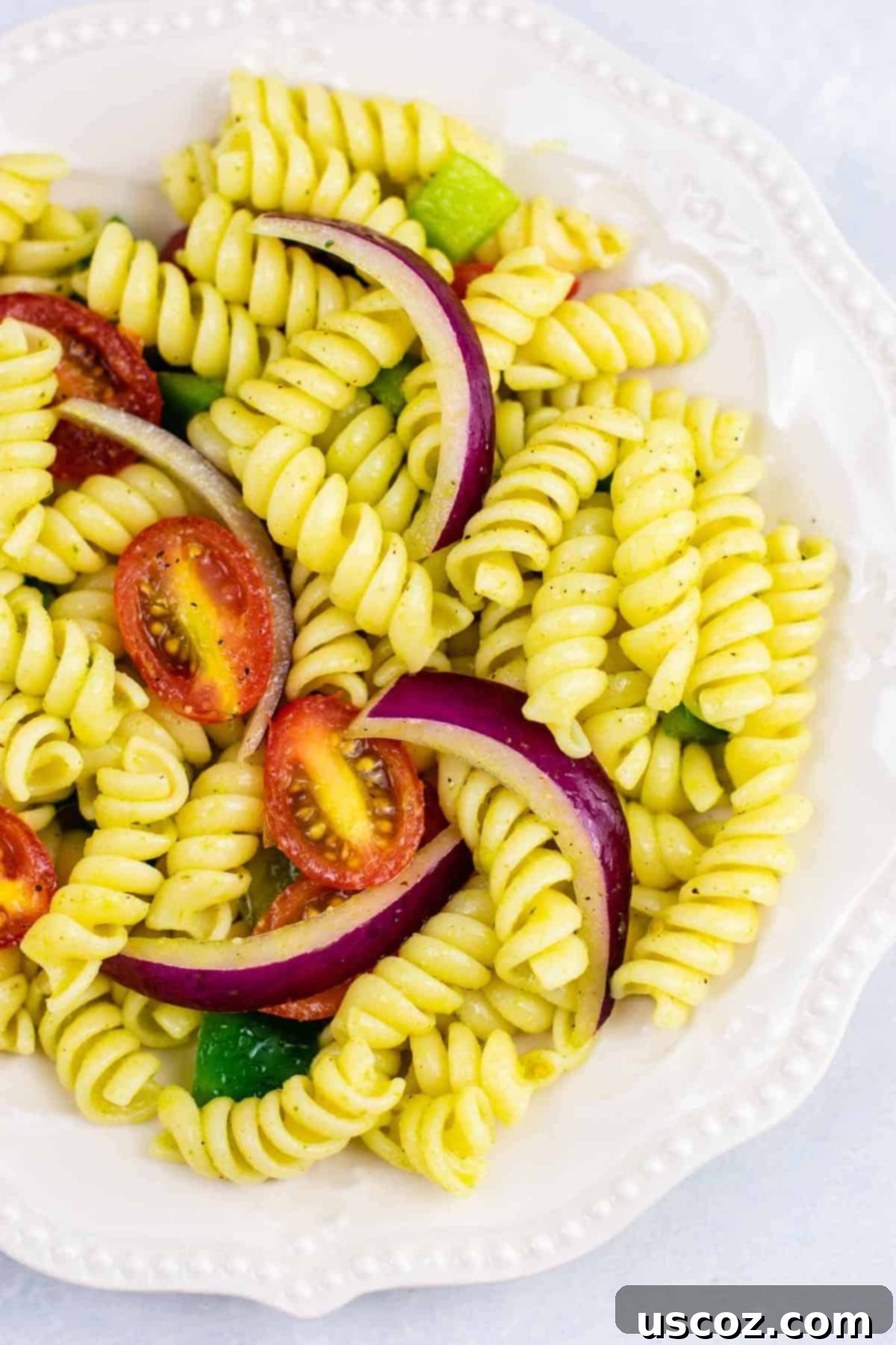 Vegan Pasta Salad 2 A vibrant bowl of vegan pasta salad with rotini pasta, cherry tomatoes, red onion, and green bell pepper, drizzled with olive oil dressing. It's an amazing, flavorful, and easy summer side dish.