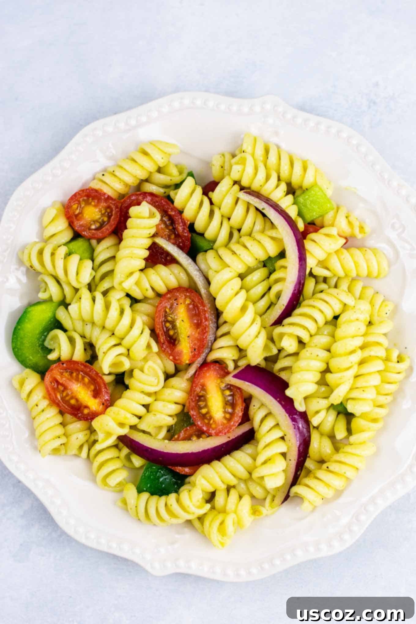 Vegan Pasta Salad 6 Mixing bowl with cooked rotini pasta, fresh vegetables, and homemade vegan dressing being tossed together for an even coating.