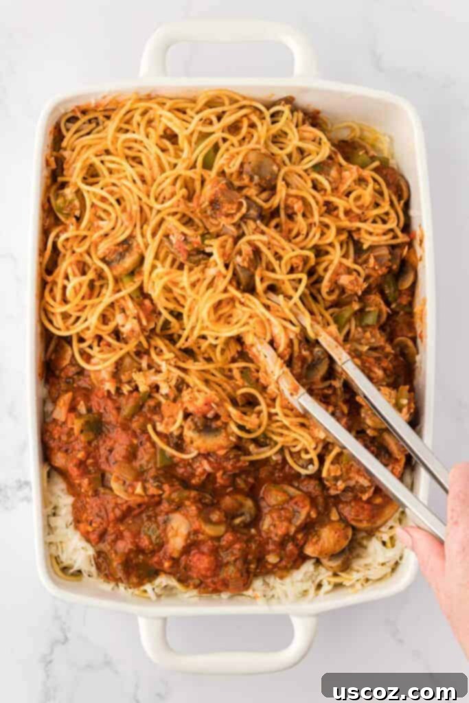 Hearty Vegetarian Spaghetti Bake 15 Mixing spaghetti with sauce and cheese using tongs in a casserole dish