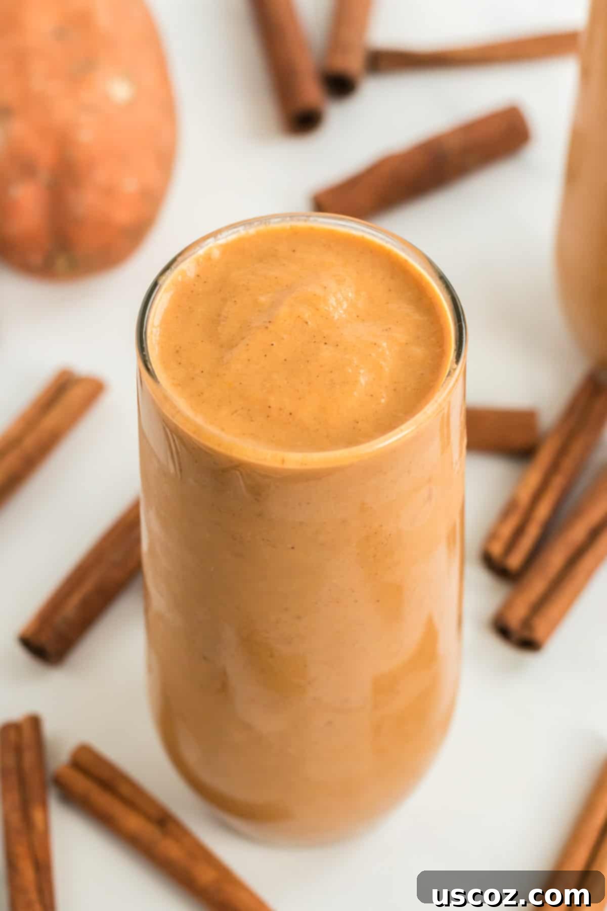 tall glass filled with sweet potato smoothie with cinnamon sticks in the background