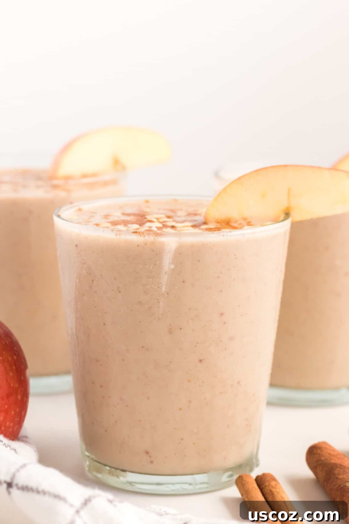 Liquid Apple Pie 8 Two glasses of apple pie smoothie, one topped with cinnamon and oats, the other with an apple slice, presented on a rustic wooden surface
