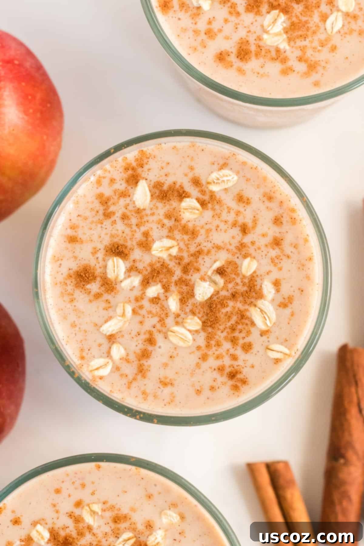 Liquid Apple Pie 9 A glass of healthy apple pie smoothie with cinnamon and oats on top, next to a bowl of fresh apple slices and a cored apple