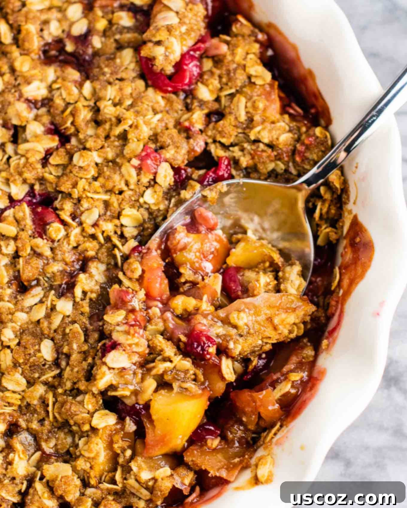 Spiced Cranberry Apple Crumble 6 A spoon scooping a generous portion of warm cranberry apple crisp from a pie dish, revealing the soft fruit and crunchy topping.