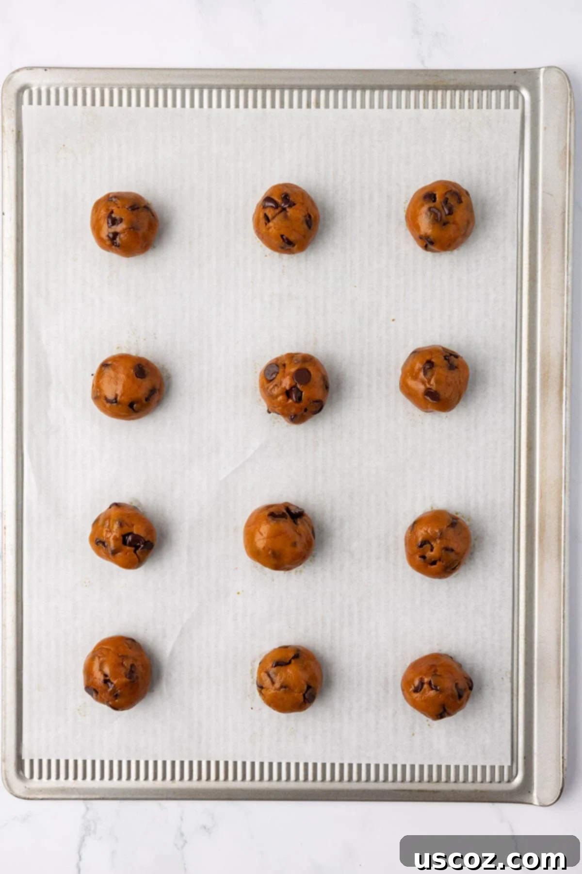 Cozy Vegan Pumpkin Chocolate Chip Cookies 13 Scoops of vegan pumpkin chocolate chip cookie dough ready for baking on a nonstick sheet.
