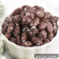Delicious chocolate covered almonds with a sprinkle of sea salt, presented in a crisp white bowl for a simple yet elegant treat.