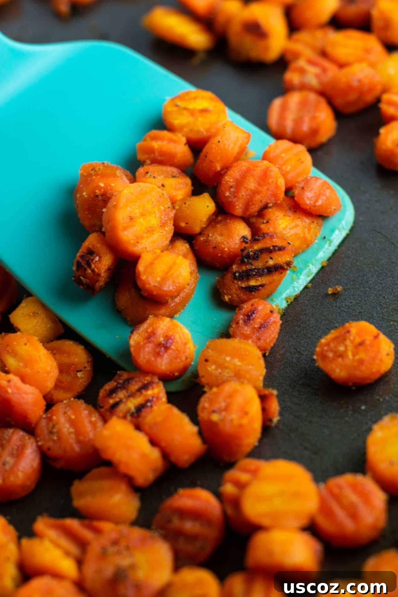 Simple & Delicious Frozen Carrot Dishes 8 A blue spatula scooping a large portion of perfectly roasted frozen carrots, showcasing their rich color and inviting texture.