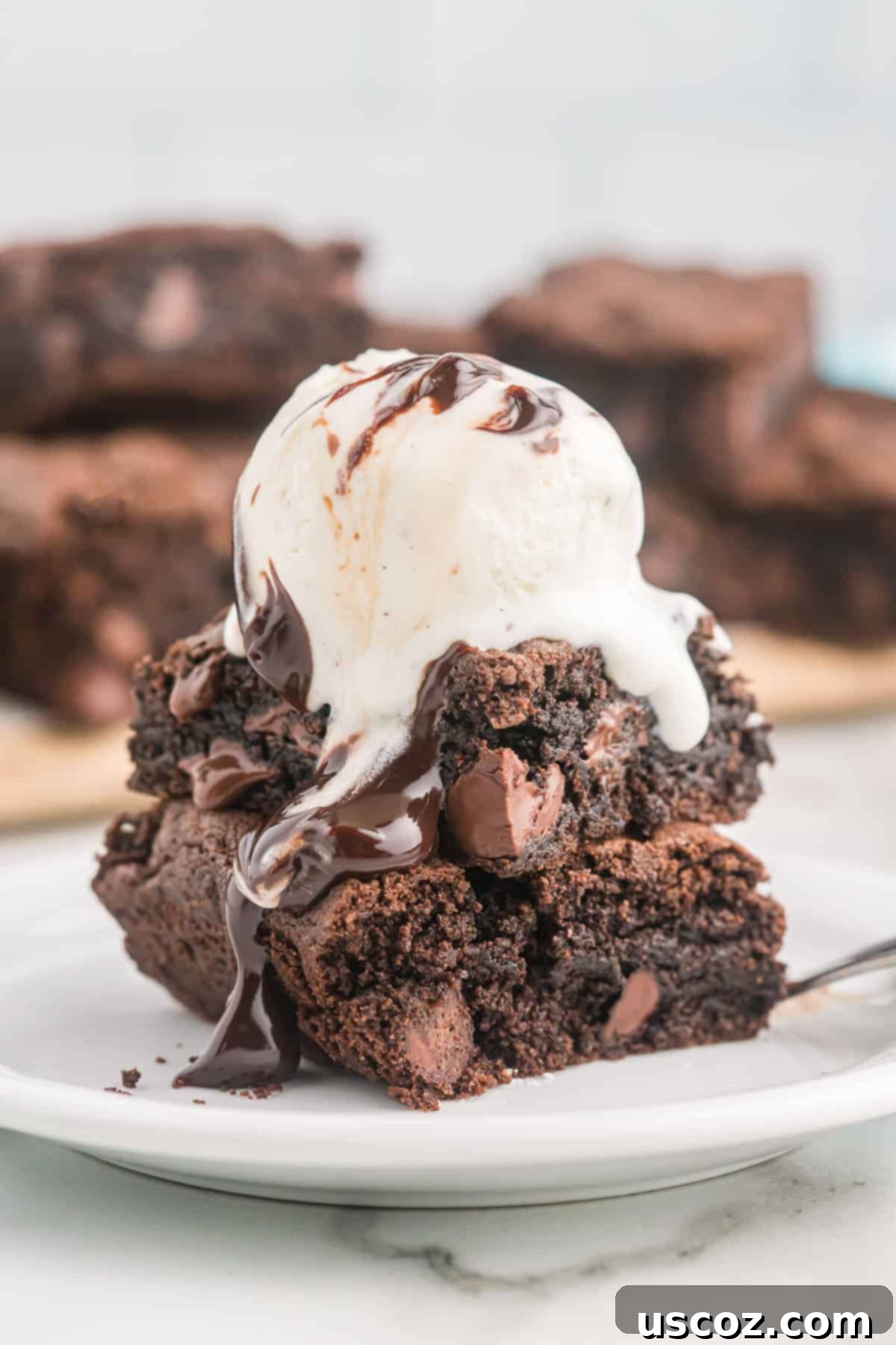 Easy Cake Mix Brownies 12 Fudgy cake mix brownies topped with a scoop of vanilla ice cream and drizzled with chocolate syrup, ready to be enjoyed.