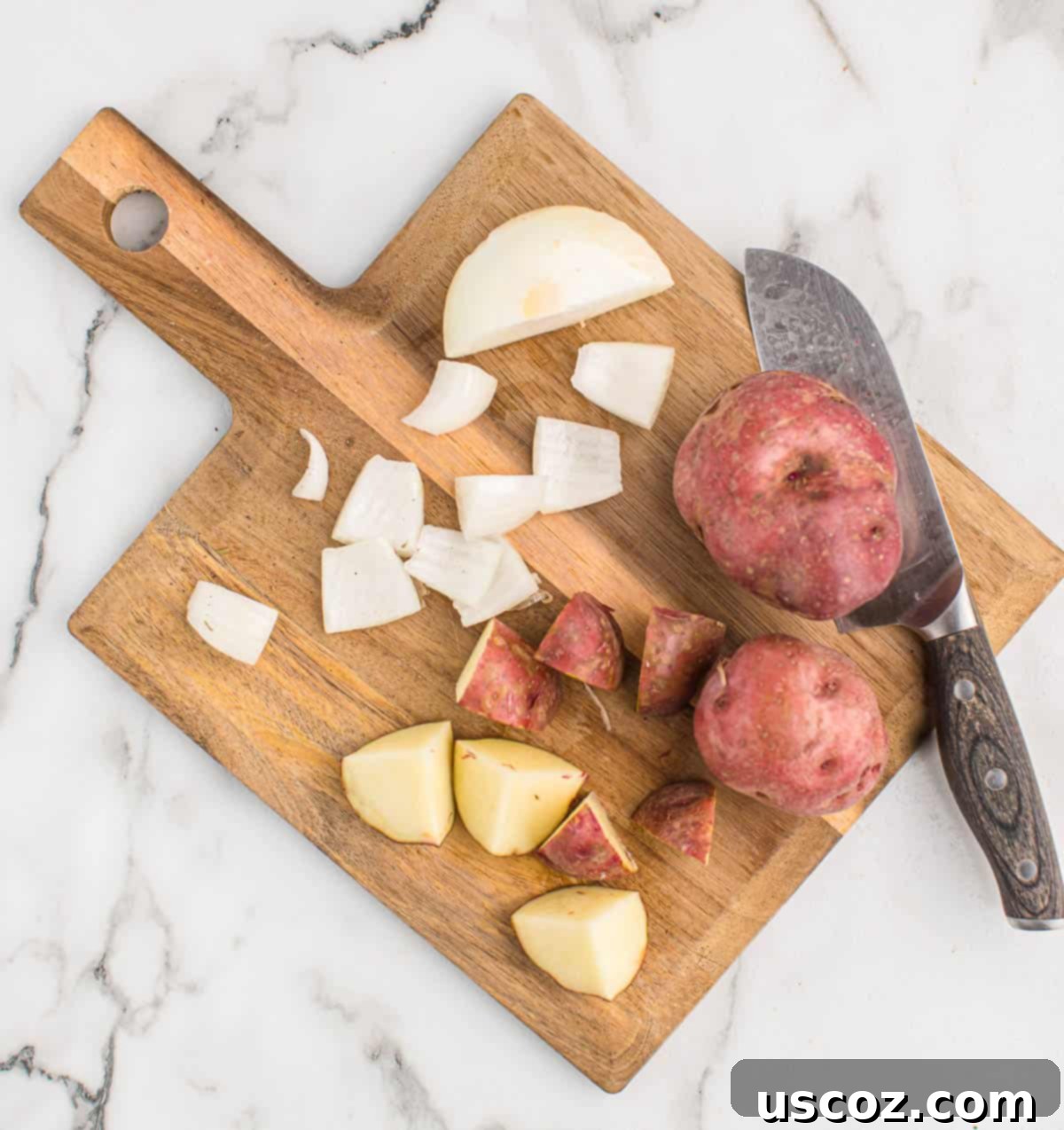Caramelized Onion and Potato Medley 7 Hands cutting red potatoes and onions on a wooden cutting board, preparing them for roasting.