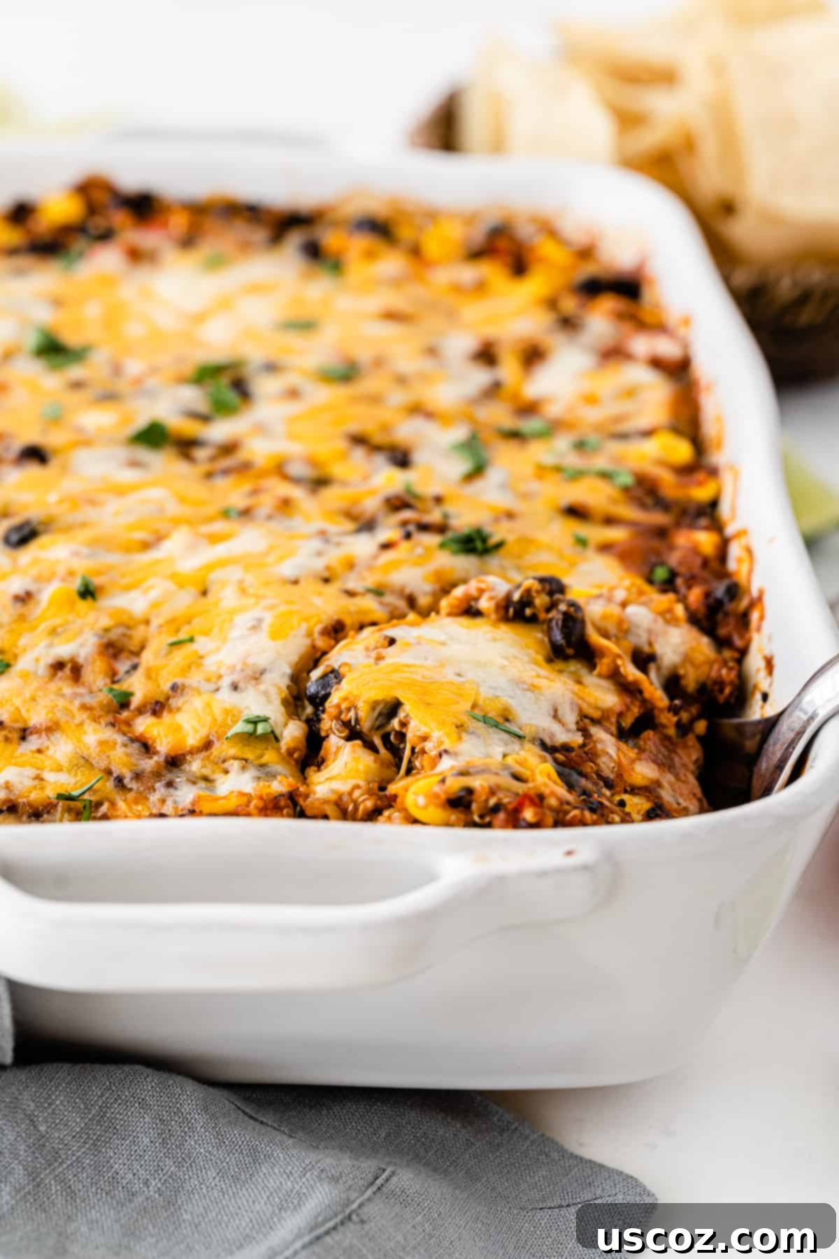Wholesome Quinoa Enchilada Bake 9 A close-up shot of Mexican quinoa casserole in a white baking dish, with a serving spoon taking a delicious scoop, highlighting its inviting texture.