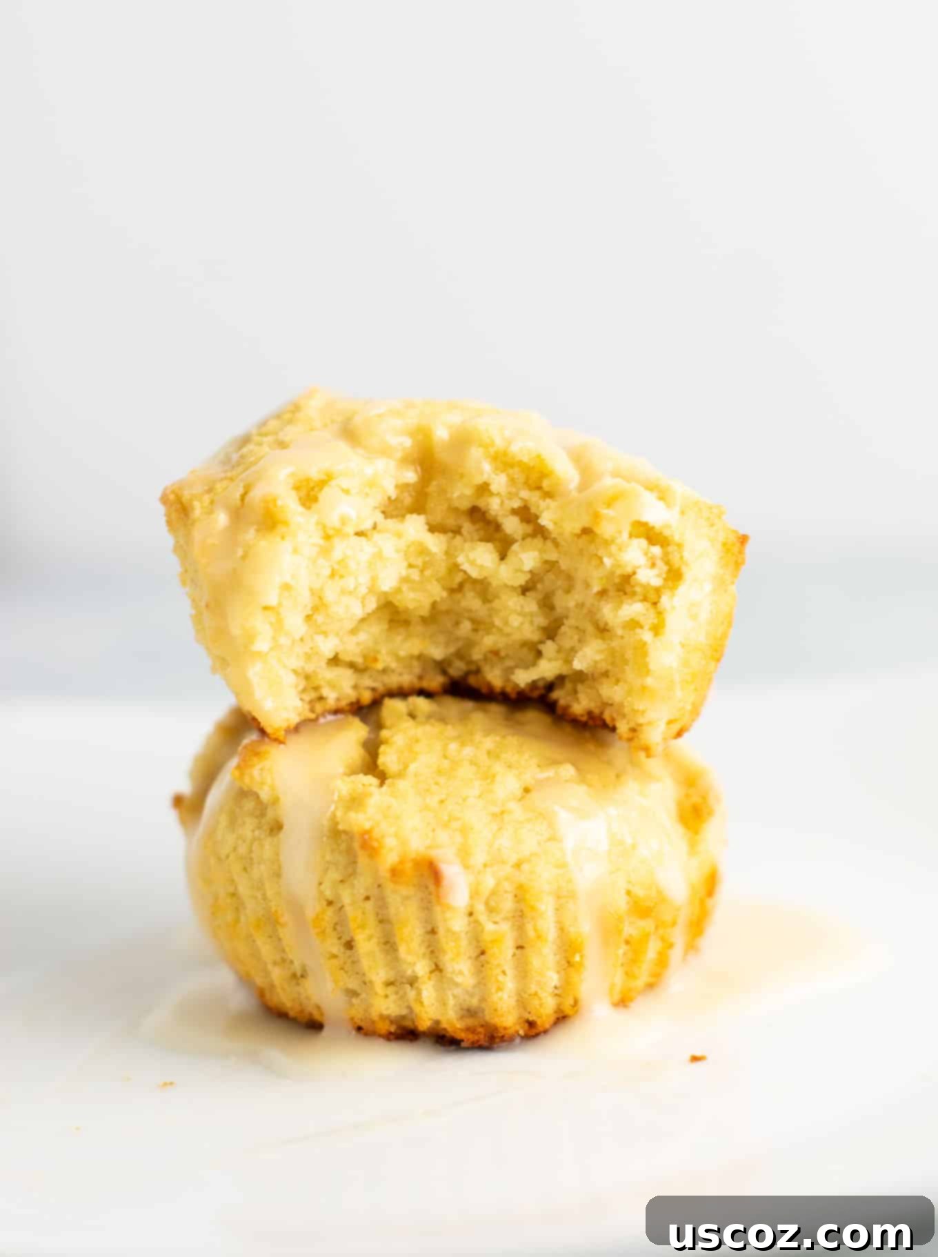 Zesty Gluten Free Lemon Muffins 7 Two gluten-free lemon muffins with a sweet glaze, one broken open to show the light and fluffy interior. #glutenfree #lemonmuffins #breakfast