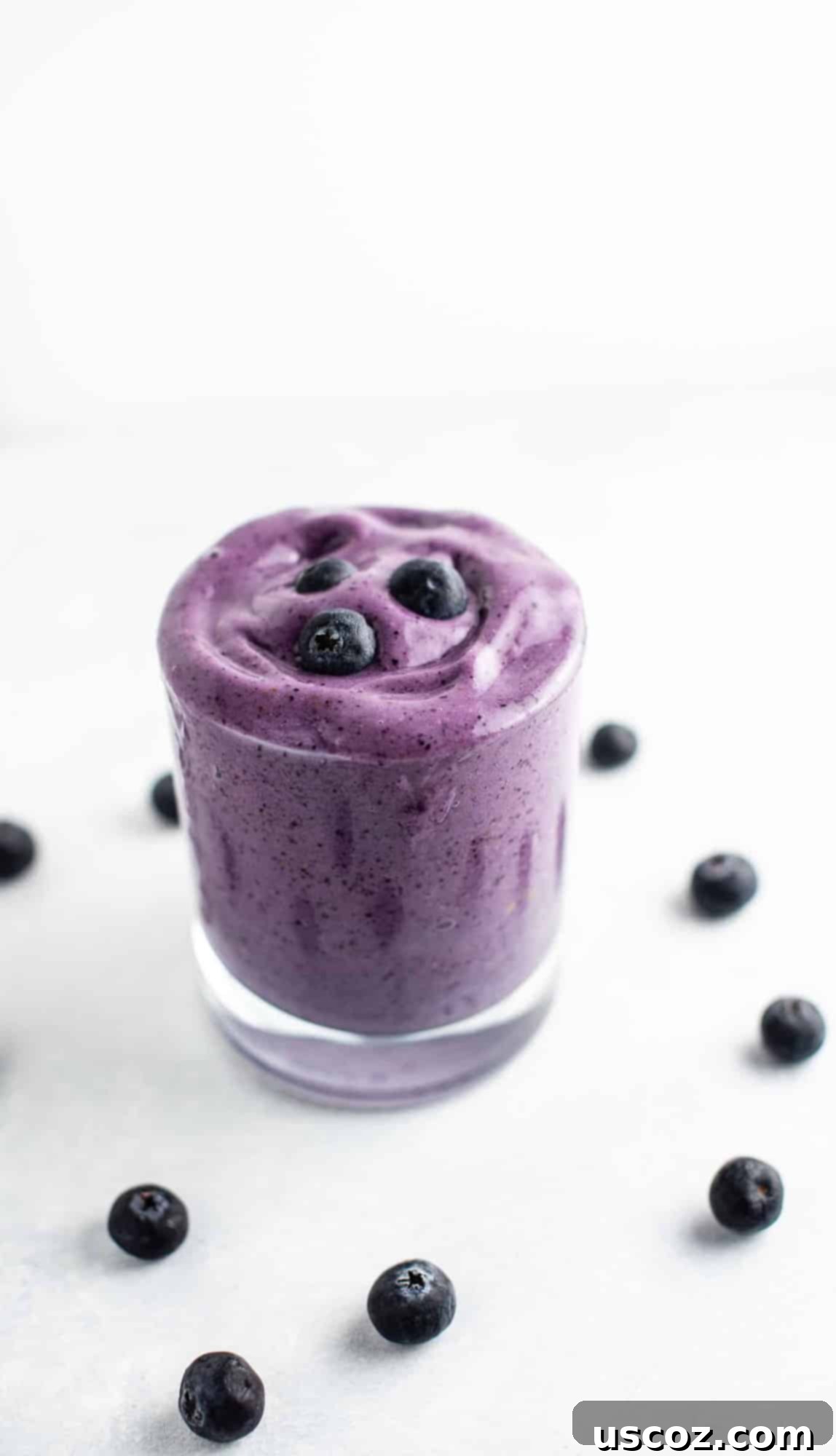 Blueberry Banana Bliss Smoothie 2 A vibrant blueberry banana smoothie in a glass, garnished with fresh blueberries around it, set against a bright background.