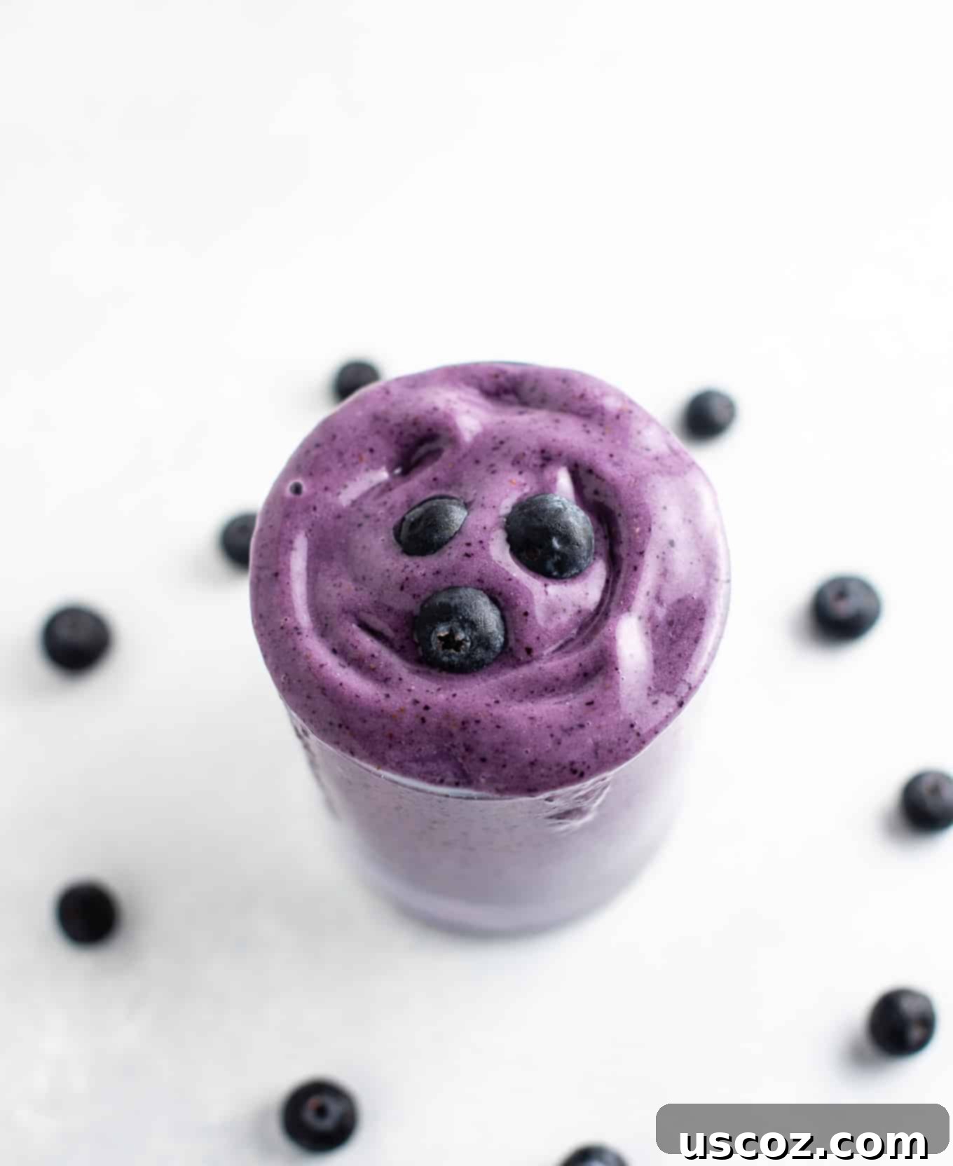 Blueberry Banana Bliss Smoothie 4 An overhead view of a blueberry smoothie in a glass, with a few fresh blueberries scattered around the base.