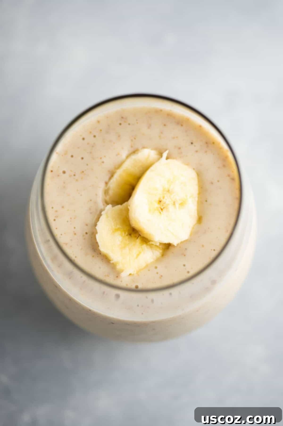 Creamy Banana Delight 2 A glass of creamy banana smoothie topped with a sliced banana, set against a bright background.