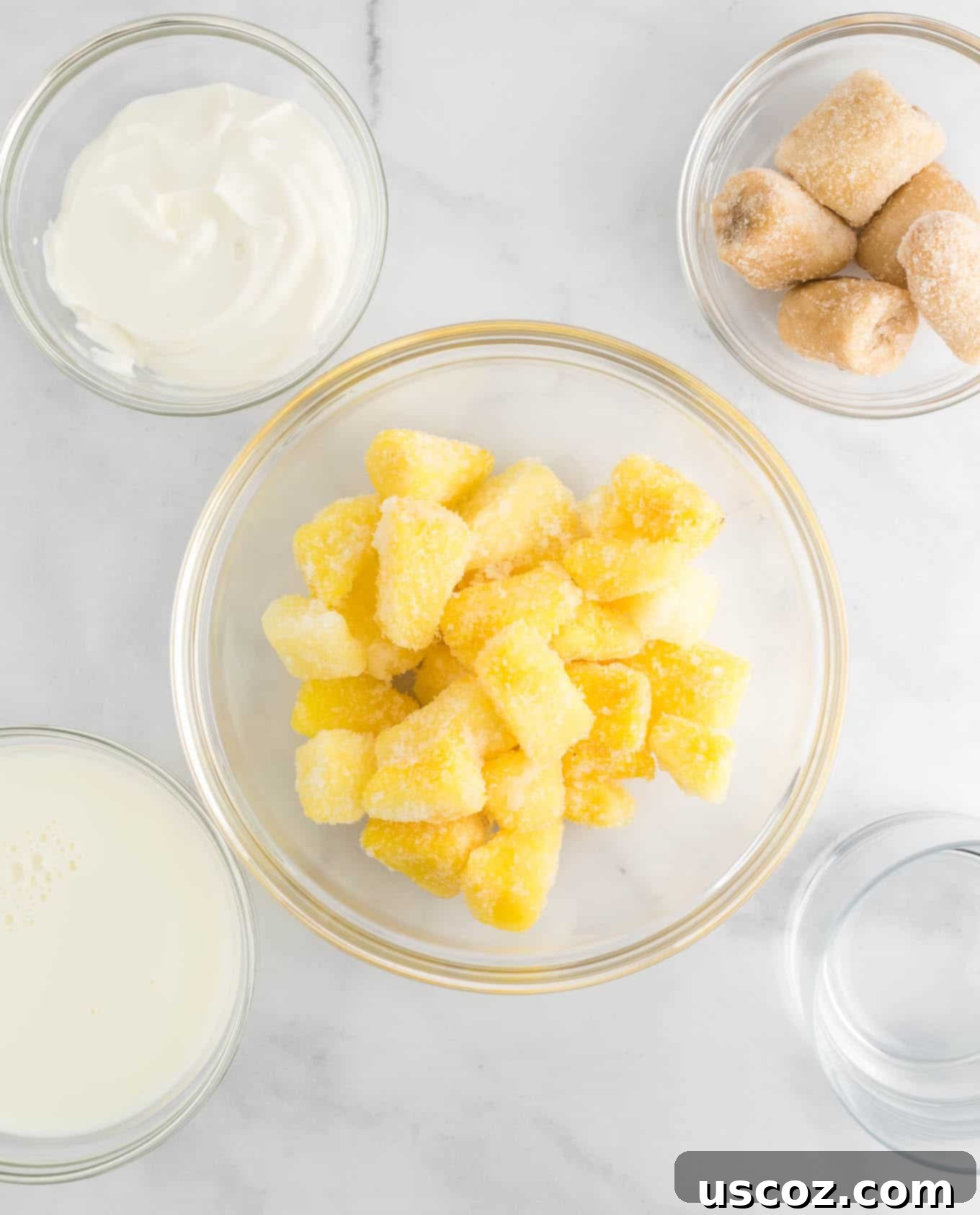 Tropical Pineapple Chill 5 the ingredients in clear bowls - frozen pineapple chunks, greek yogurt, frozen banana chunks, and milk